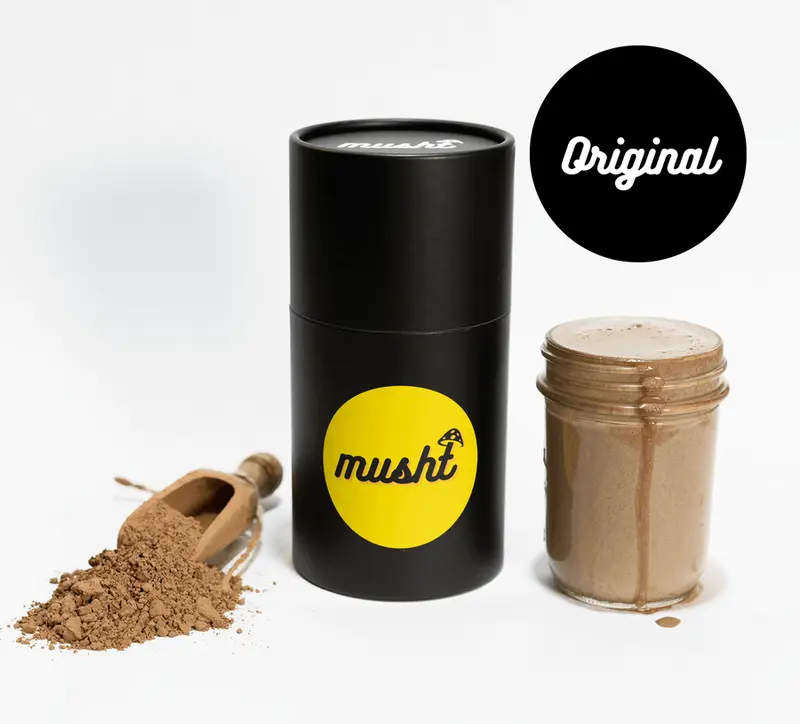 Musht Original drink mix beside a creamy blended drink and a wooden scoop